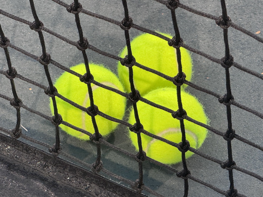 Three tennis balls behind a net.